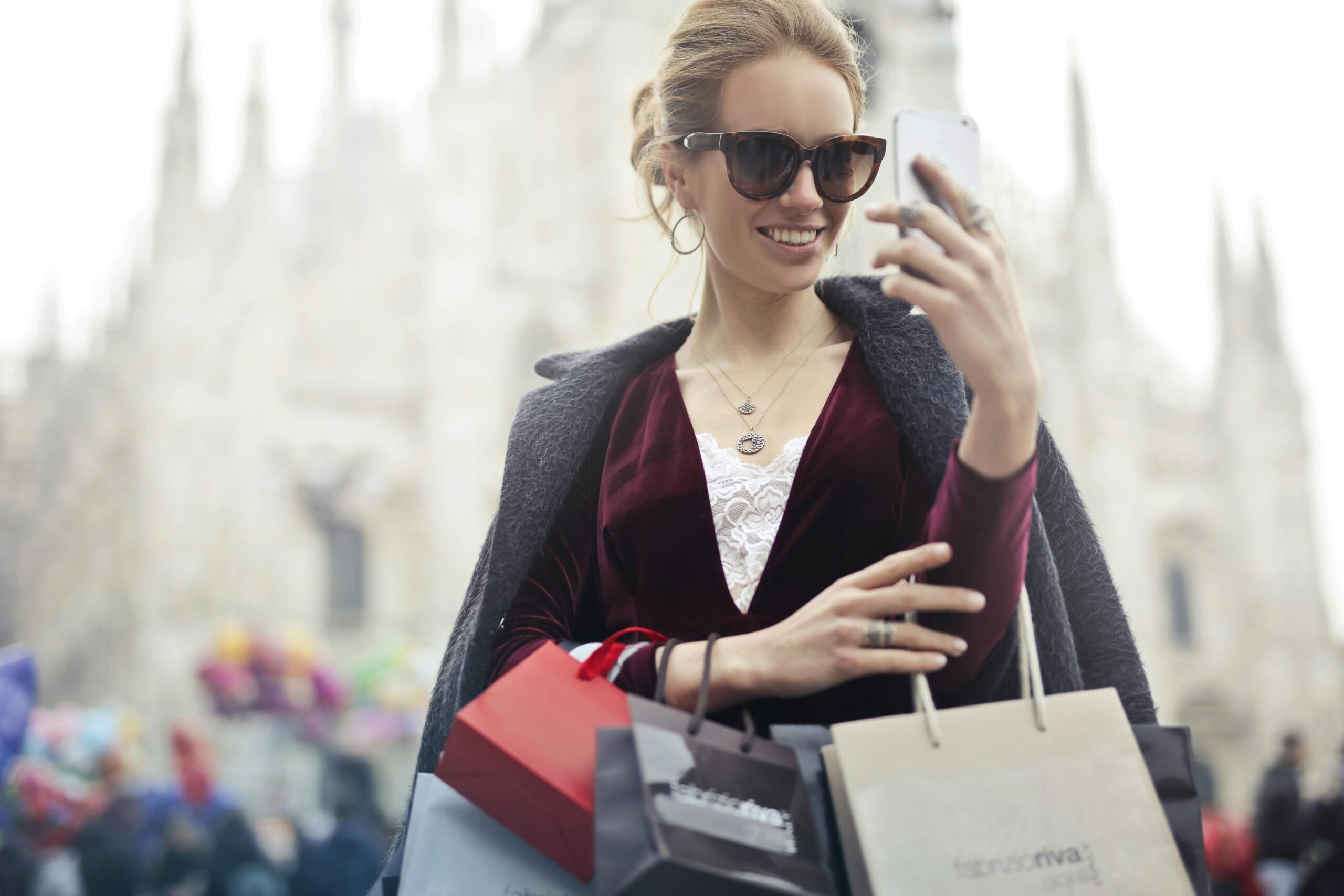 Young woman looking at cell phone while in Europe and holding several shopping bags